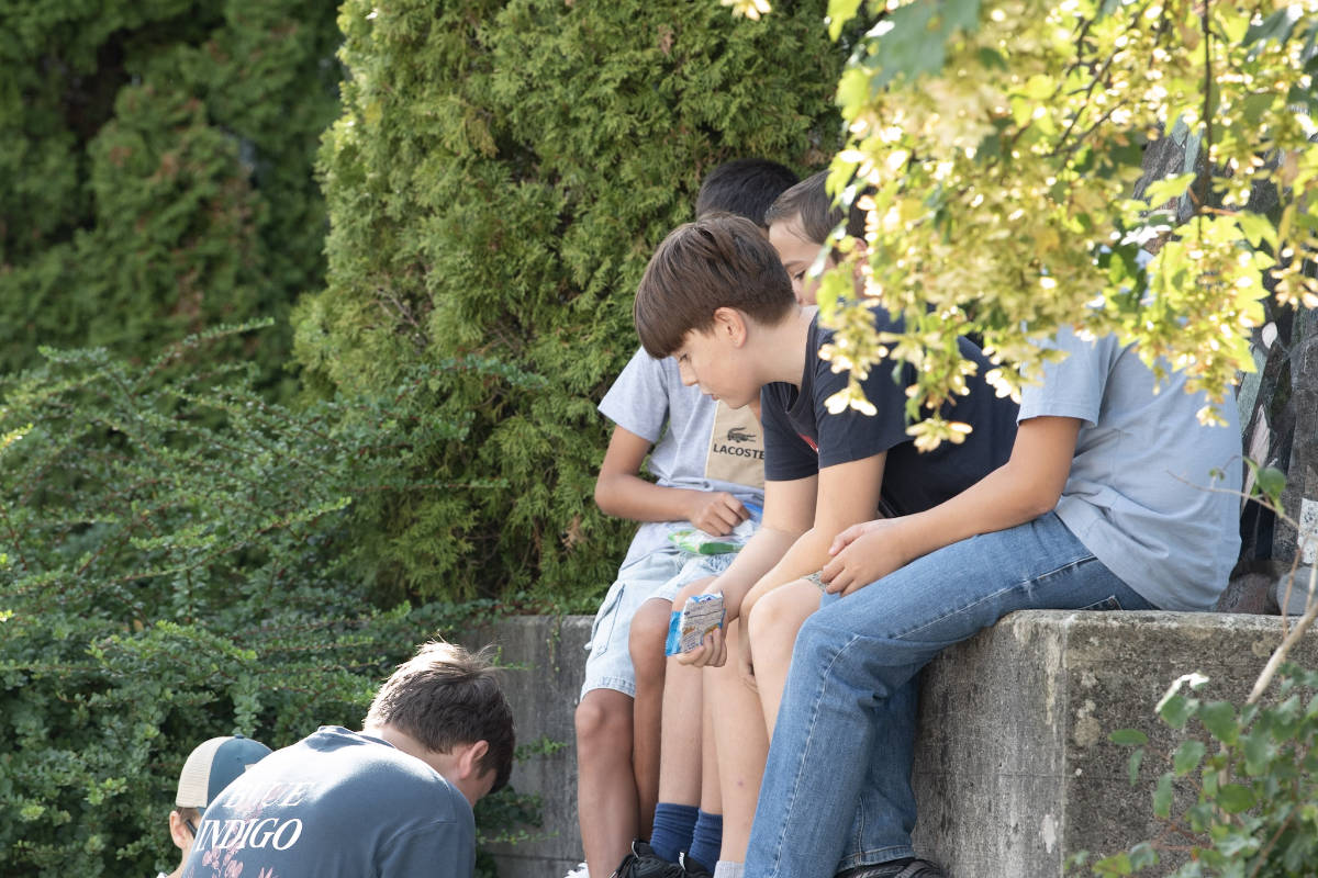Schulkinder sitzen in der Pause auf einer Mauer und essen ihren Znüni
