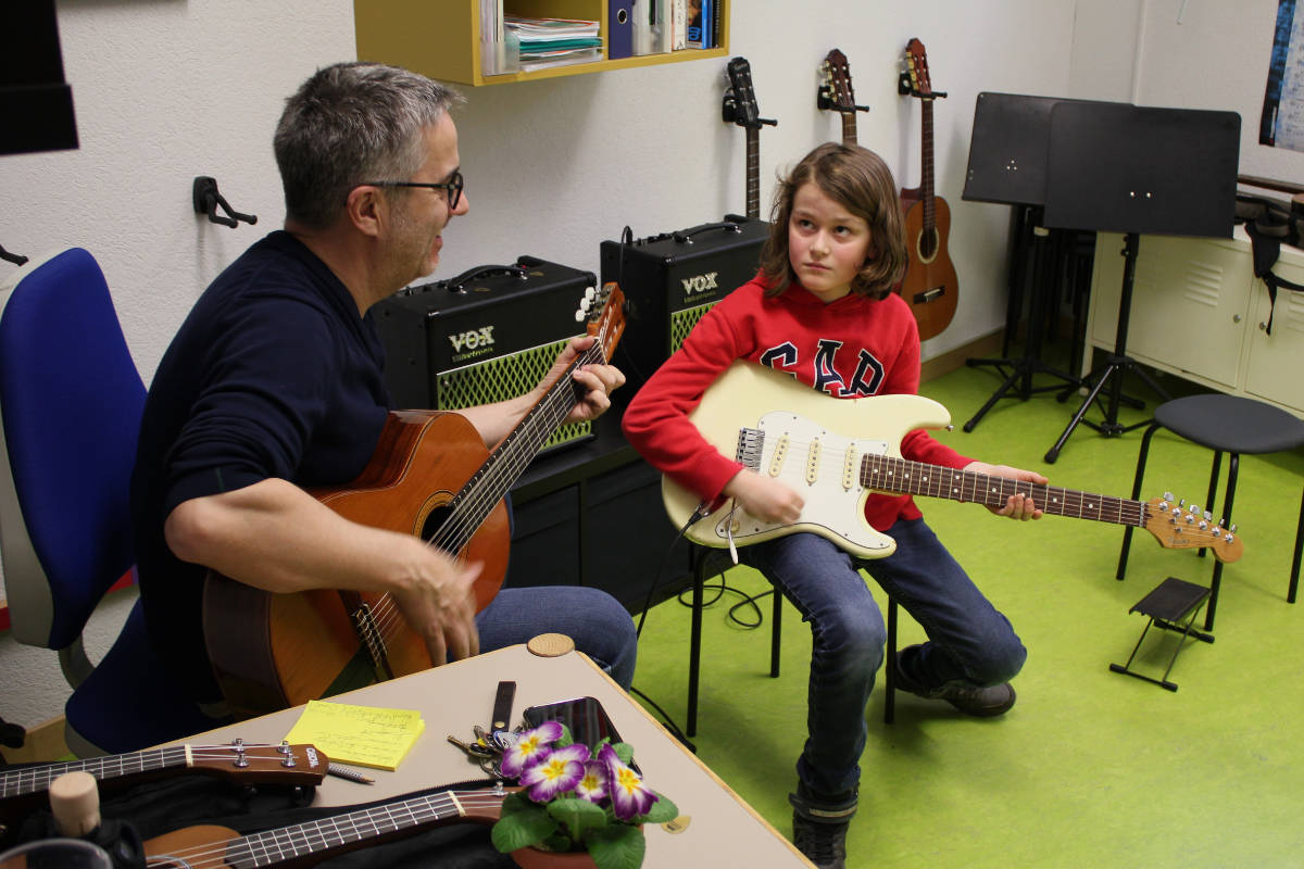 Gitarrenunterricht: Lehrer an der Akustikgitarre, Schüler an der E-Gitarre