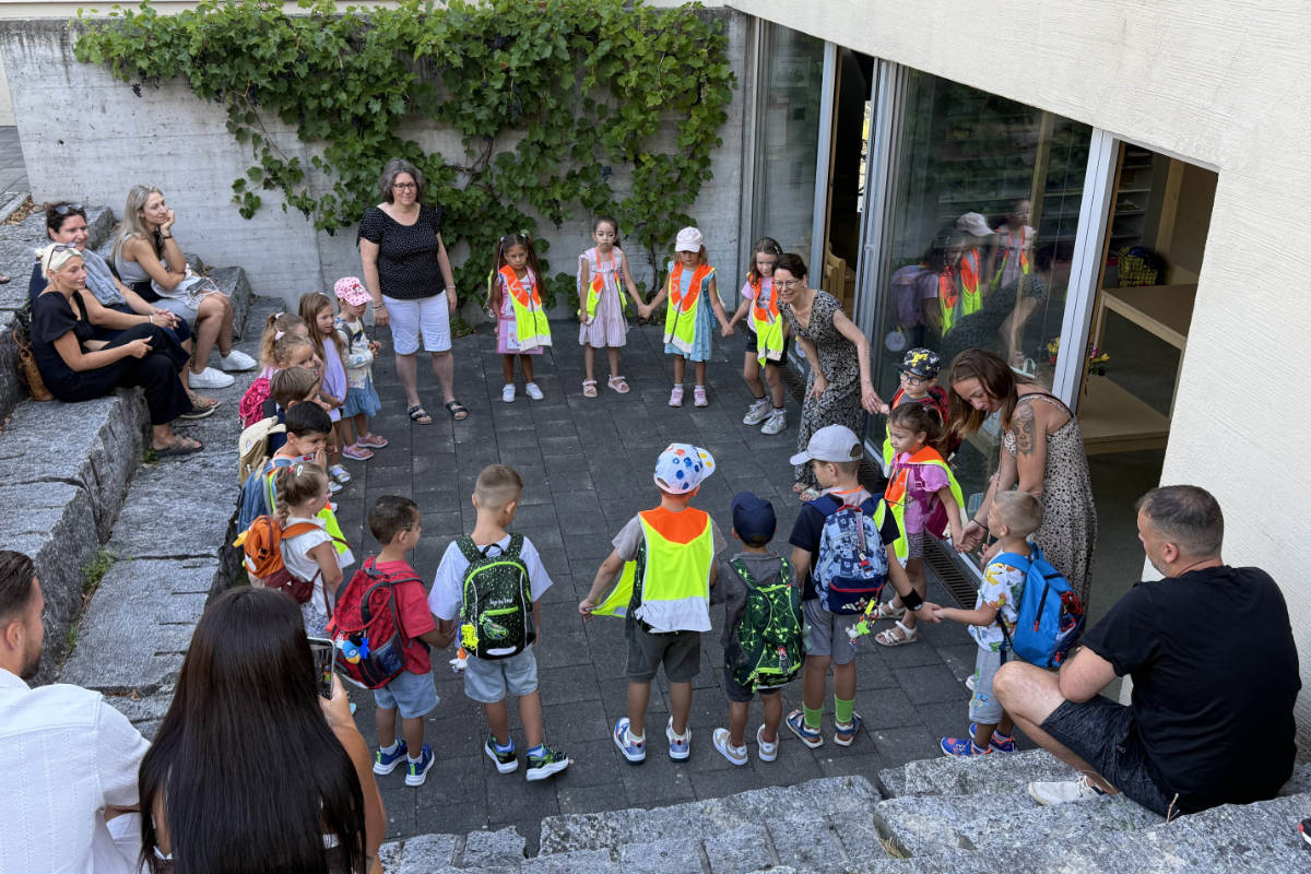 Kinder mit Leuchtwesten und Rucksäcken bilden vor dem Kindergarten einen Kreis