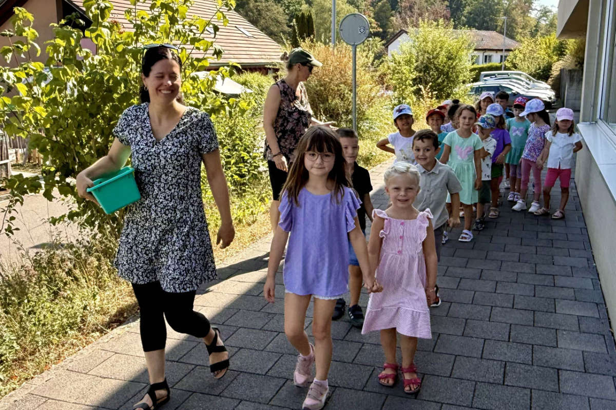 Kindergartengruppe unterwegs auf dem Trottoir, begleitet von zwei Lehrpersonen
