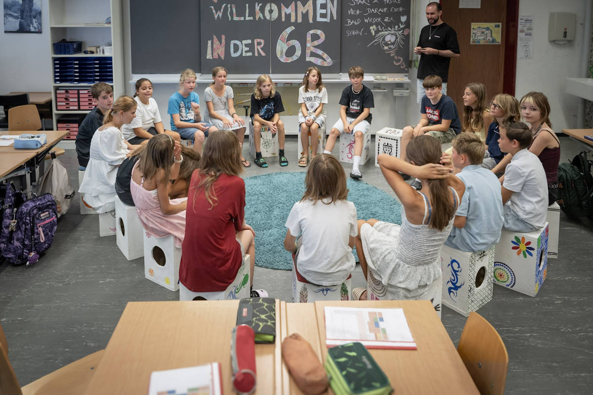 Primarklasse im Sitzkreis vor der Wandtafel mit Willkommensgruss
