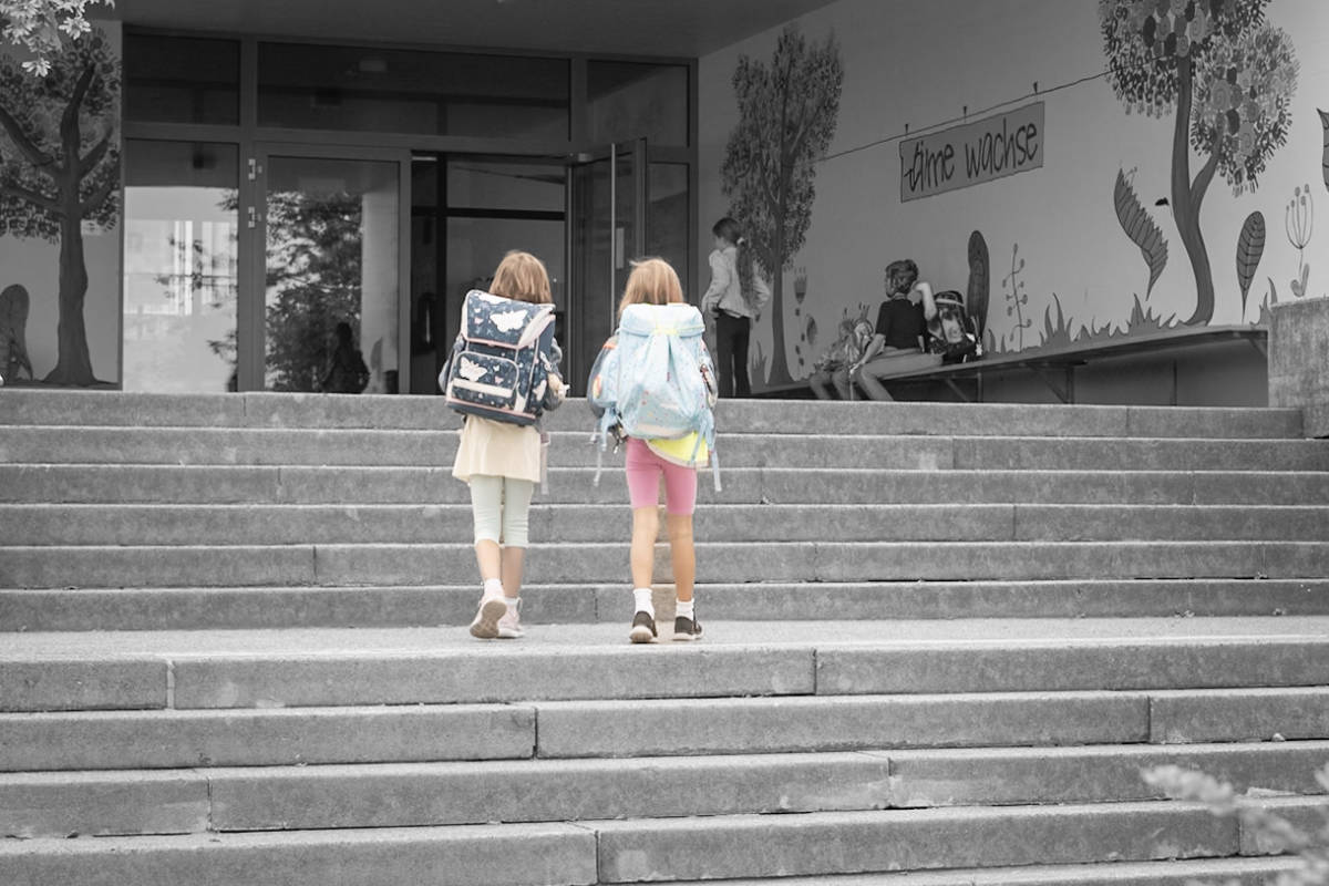 Zwei Mädchen mit Schulranzen steigen die Treppe zum Schulhauseingang hoch
